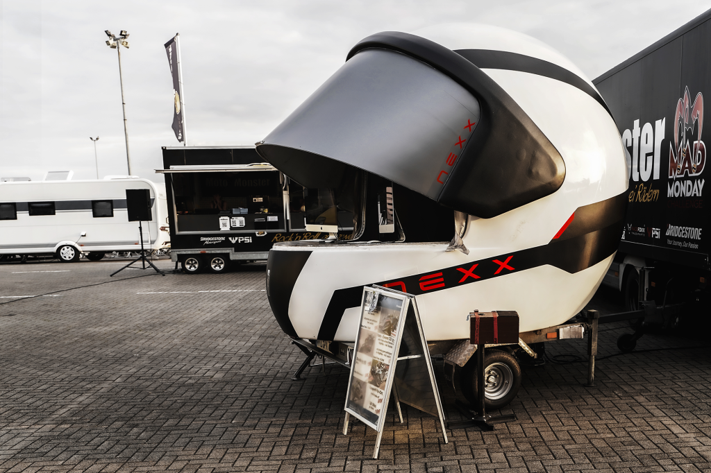 Capacete gigante NEXX sendo transportado por uma estrada europeia, simbolizando a jornada e a aventura do motociclismo.