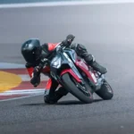 Motociclistas em curso de pilotagem na Ultraviolette Riding Academy com motocicletas elétricas da marca em pista de asfalto, sob a supervisão de instrutores.