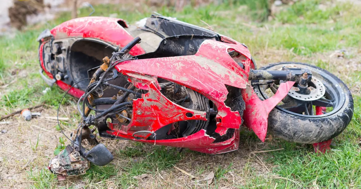 Mecânico inspecionando o chassi de uma moto usada em busca de sinais de solda ou recuperação após acidente, com ferramentas e ambiente de oficina ao fundo.