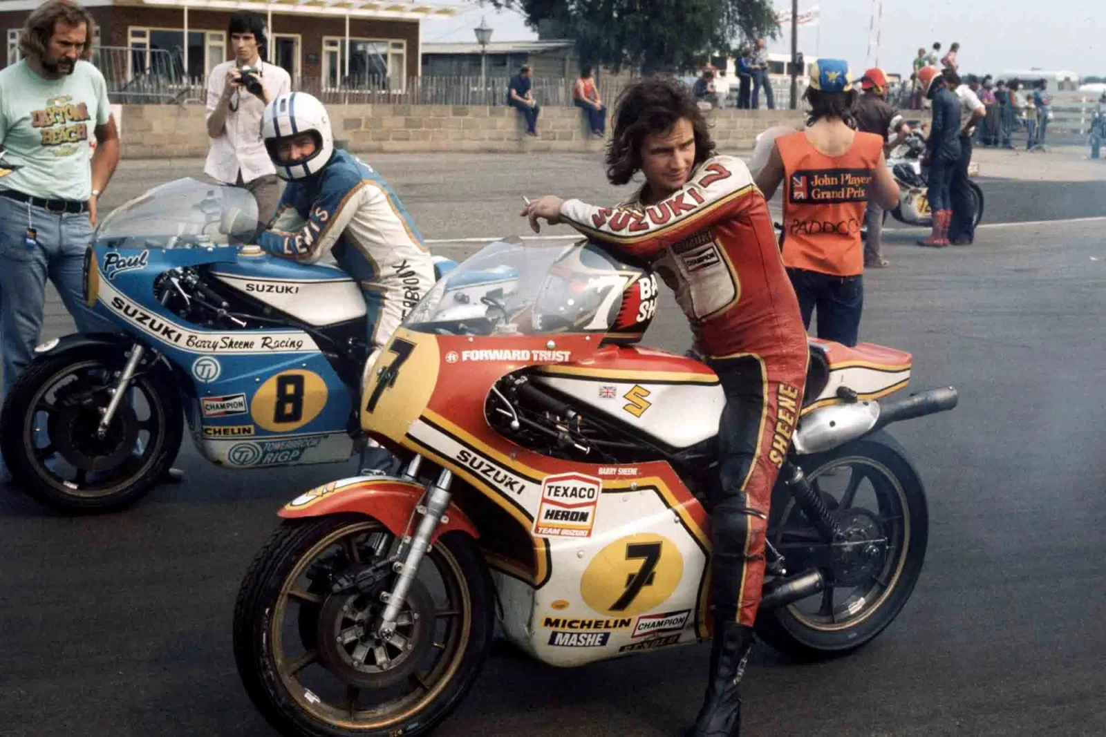 Barry Sheene pilotando a icônica Suzuki RG500 de dois tempos durante uma corrida de Grande Prêmio na década de 1970, destacando a agressividade e velocidade da máquina.