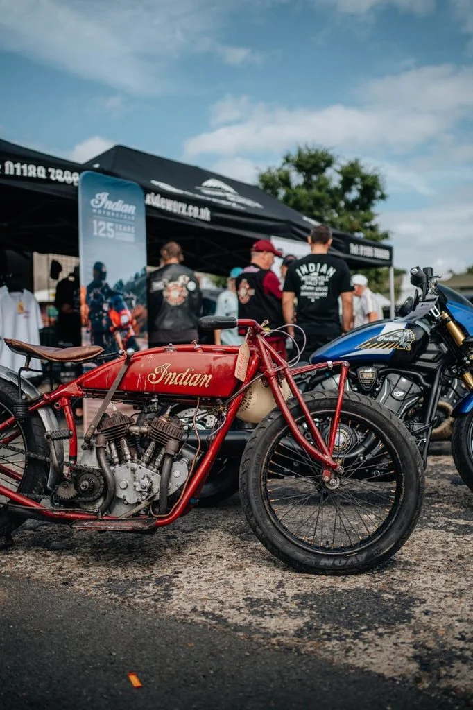 Motocicletas Indian de diversas épocas reunidas em frente ao histórico Brooklands Museum, celebrando os 125 anos da marca, com a pista de corrida ao fundo.