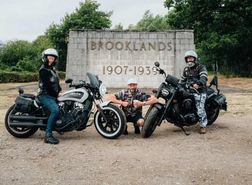 Motocicletas Indian de diversas épocas reunidas em frente ao histórico Brooklands Museum, celebrando os 125 anos da marca, com a pista de corrida ao fundo.