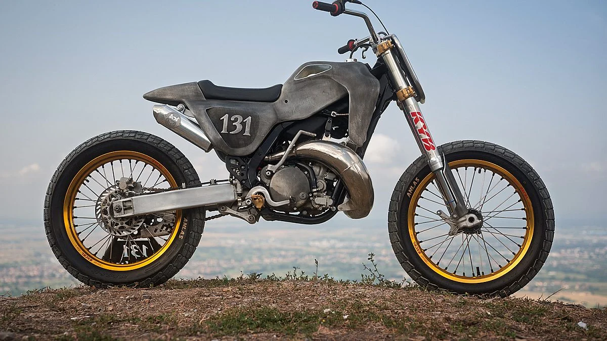 Kawasaki KX250 custom com carroceria de alumínio superleggera, exibindo estrutura tubular e acabamento escuro sem pintura