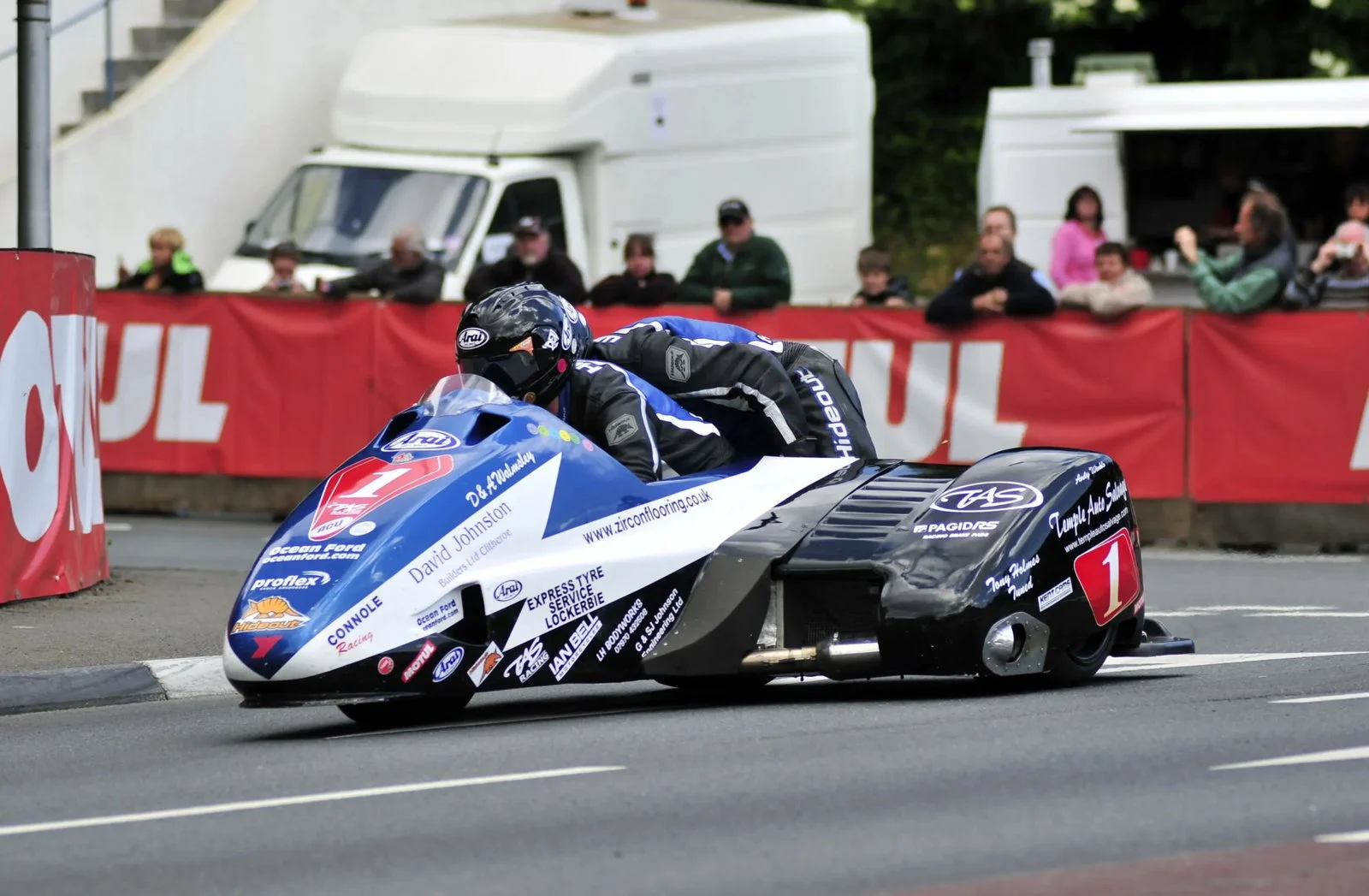 Uma dupla de sidecar em alta velocidade no Isle of Man TT, mostrando a complexidade e a adrenalina da corrida.