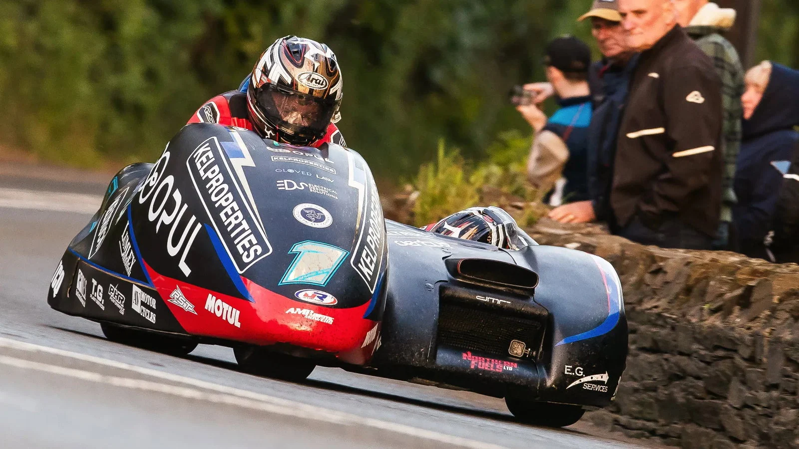 Uma dupla de sidecar em alta velocidade no Isle of Man TT, mostrando a complexidade e a adrenalina da corrida.