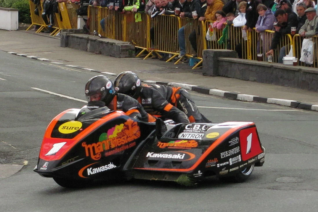 Uma dupla de sidecar em alta velocidade no Isle of Man TT, mostrando a complexidade e a adrenalina da corrida.