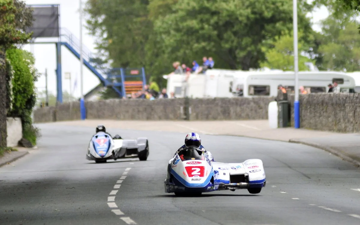 Uma dupla de sidecar em alta velocidade no Isle of Man TT, mostrando a complexidade e a adrenalina da corrida.