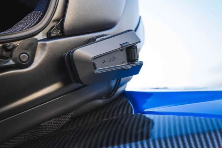 Imagem detalhada de um comunicador Cardo PACKTALK Edge montado em um capacete de motociclismo, destacando seu design moderno e botões de controle.