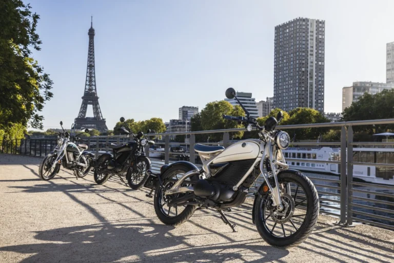 Motocicleta elétrica Royal Enfield Flying Flea C6 em destaque, exibindo seu design moderno e compacto, com farol redondo e suspensão dianteira girder, em ambiente urbano.
