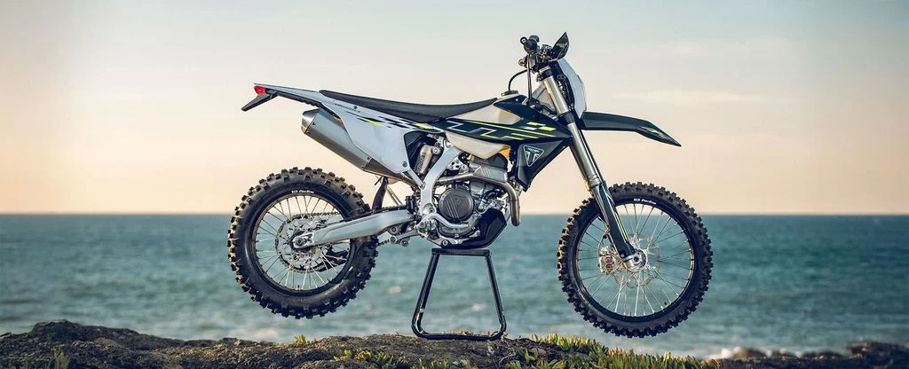 Renato Silva, campeão de Enduro, posa ao lado da nova Triumph TF 250-E em ambiente off-road, marcando a entrada da marca britânica no Enduro nacional.
