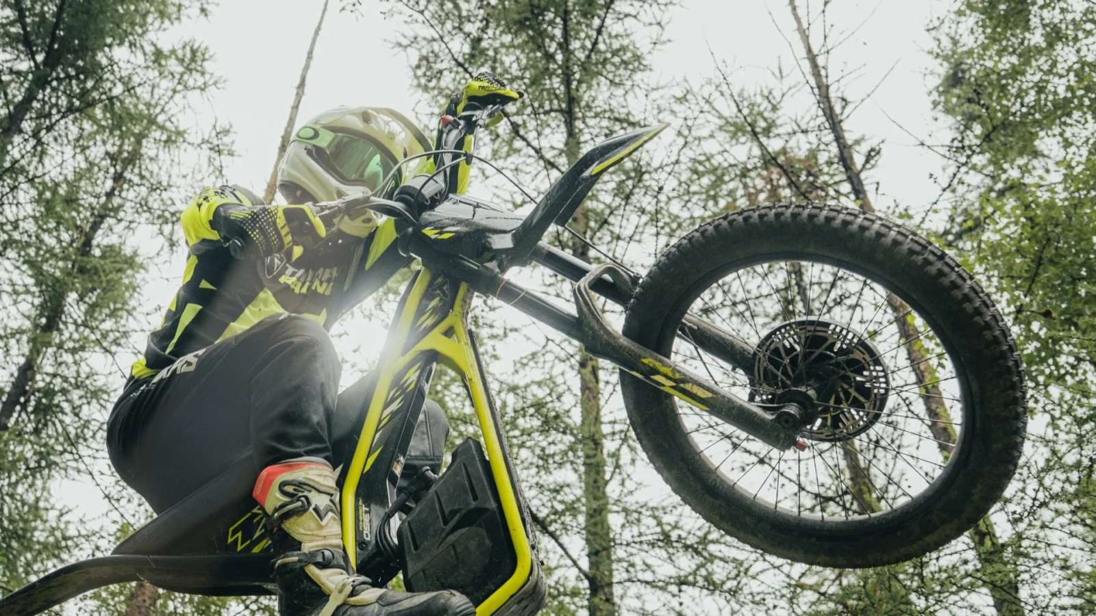 Triumph TXP 20 em ação, em um cenário de trilha com obstáculos naturais, exibindo sua agilidade e design específico para trials.