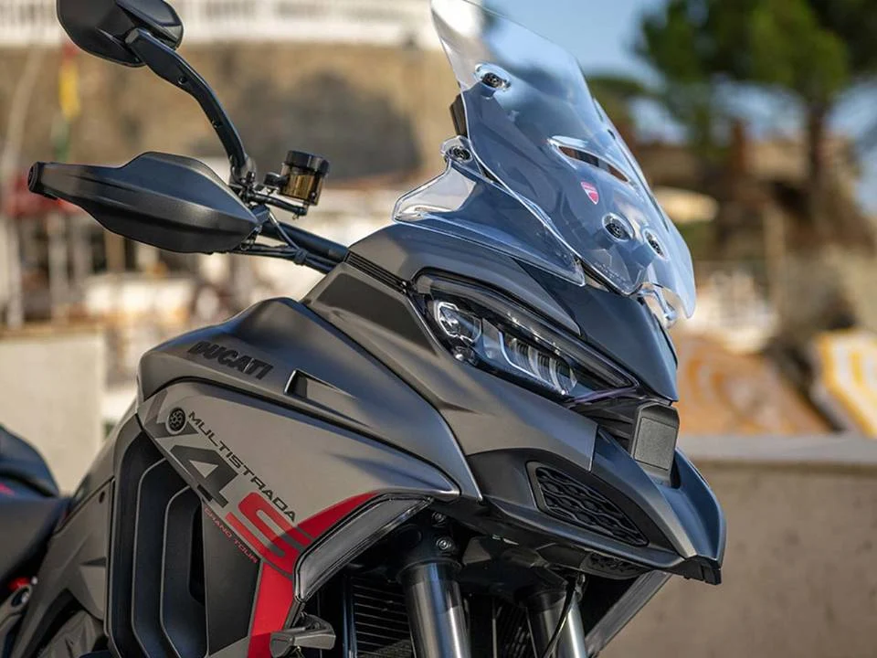 Ducati Multistrada V4 S Grand Tour 2024 em vermelho com malas laterais e detalhes em preto, estacionada em estrada europeia.
