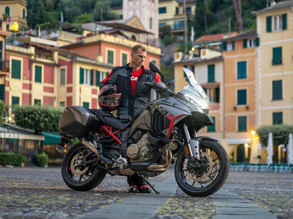 Ducati Multistrada V4 S Grand Tour 2024 em vermelho com malas laterais e detalhes em preto, estacionada em estrada europeia.