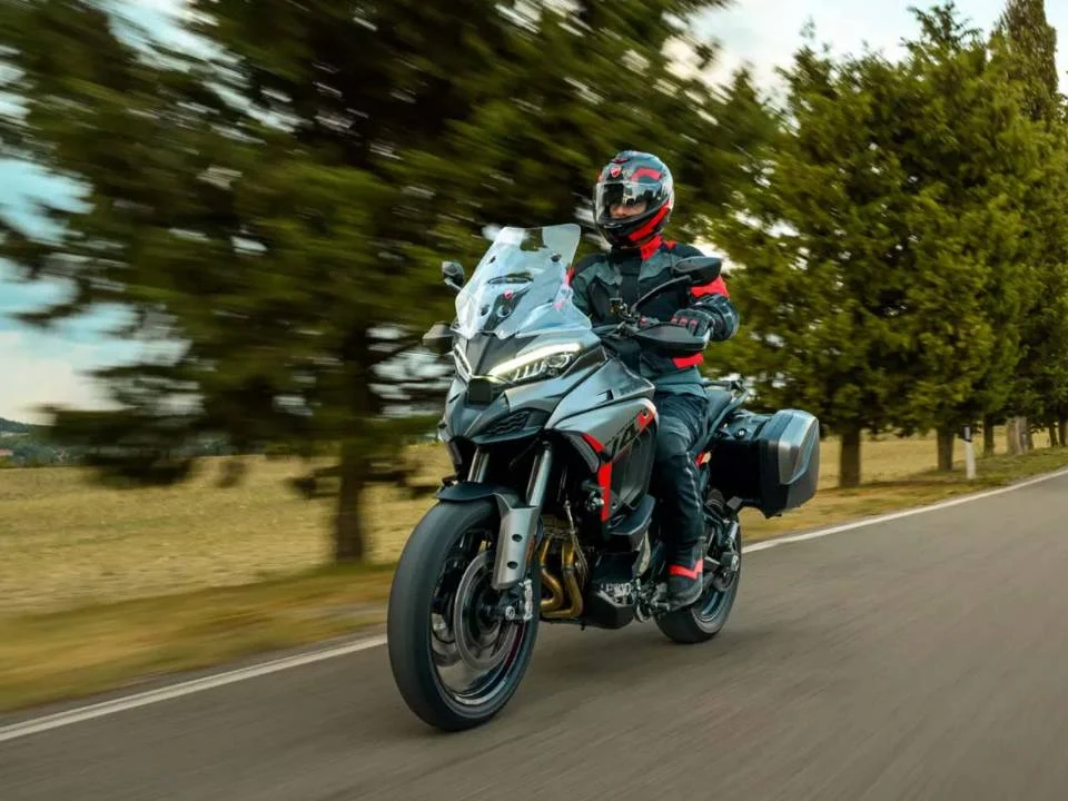 Ducati Multistrada V4 S Grand Tour 2024 em vermelho com malas laterais e detalhes em preto, estacionada em estrada europeia.
