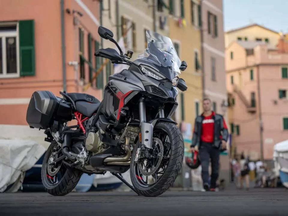 Ducati Multistrada V4 S Grand Tour 2024 em vermelho com malas laterais e detalhes em preto, estacionada em estrada europeia.