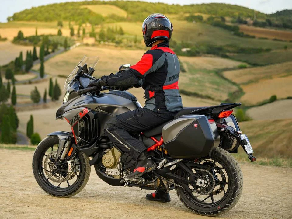Ducati Multistrada V4 S Grand Tour 2024 em vermelho com malas laterais e detalhes em preto, estacionada em estrada europeia.