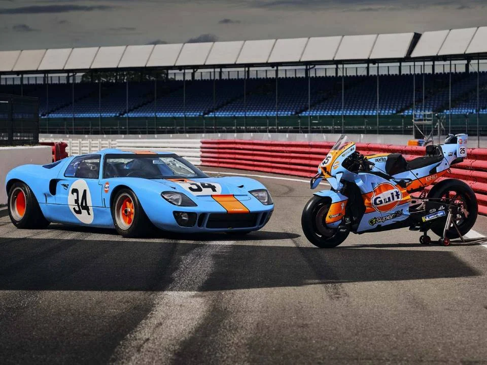 Aprilia RS-GP26 com pintura azul-claro e laranja inspirada na Ford GT40 em pista de MotoGP
