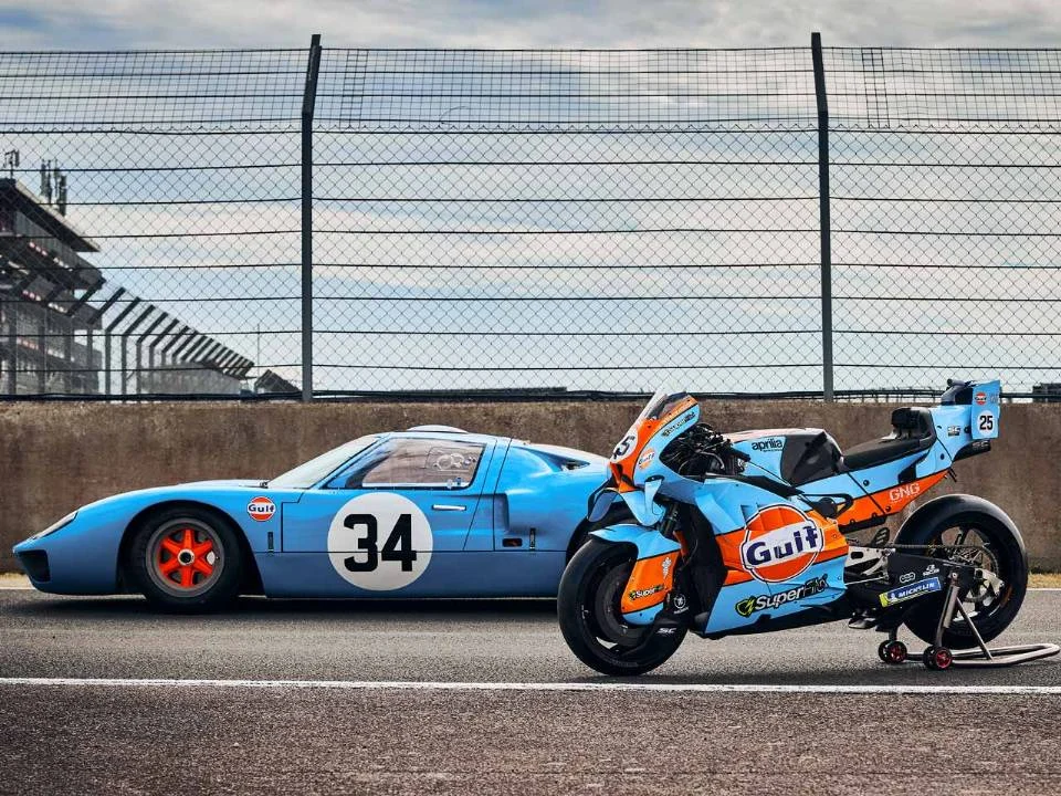Aprilia RS-GP26 com pintura azul-claro e laranja inspirada na Ford GT40 em pista de MotoGP