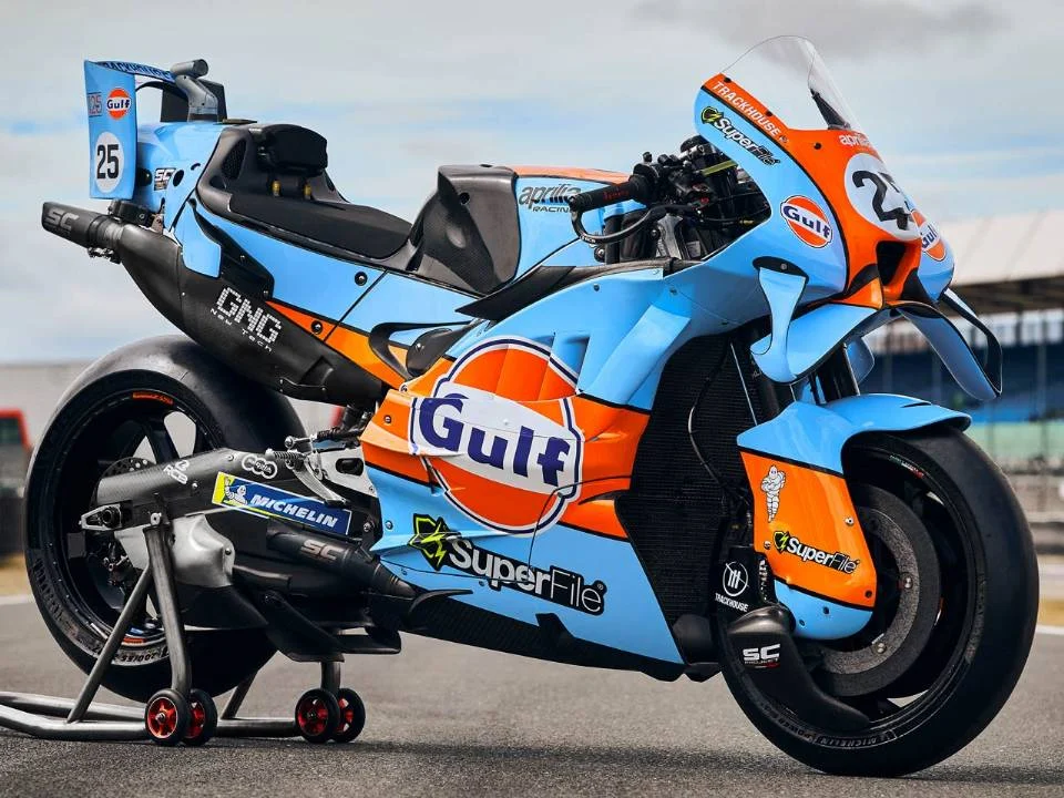 Aprilia RS-GP26 com pintura azul-claro e laranja inspirada na Ford GT40 em pista de MotoGP