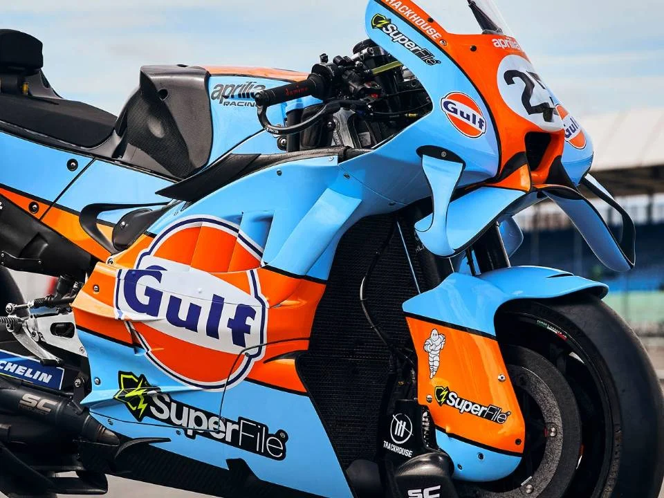 Aprilia RS-GP26 com pintura azul-claro e laranja inspirada na Ford GT40 em pista de MotoGP