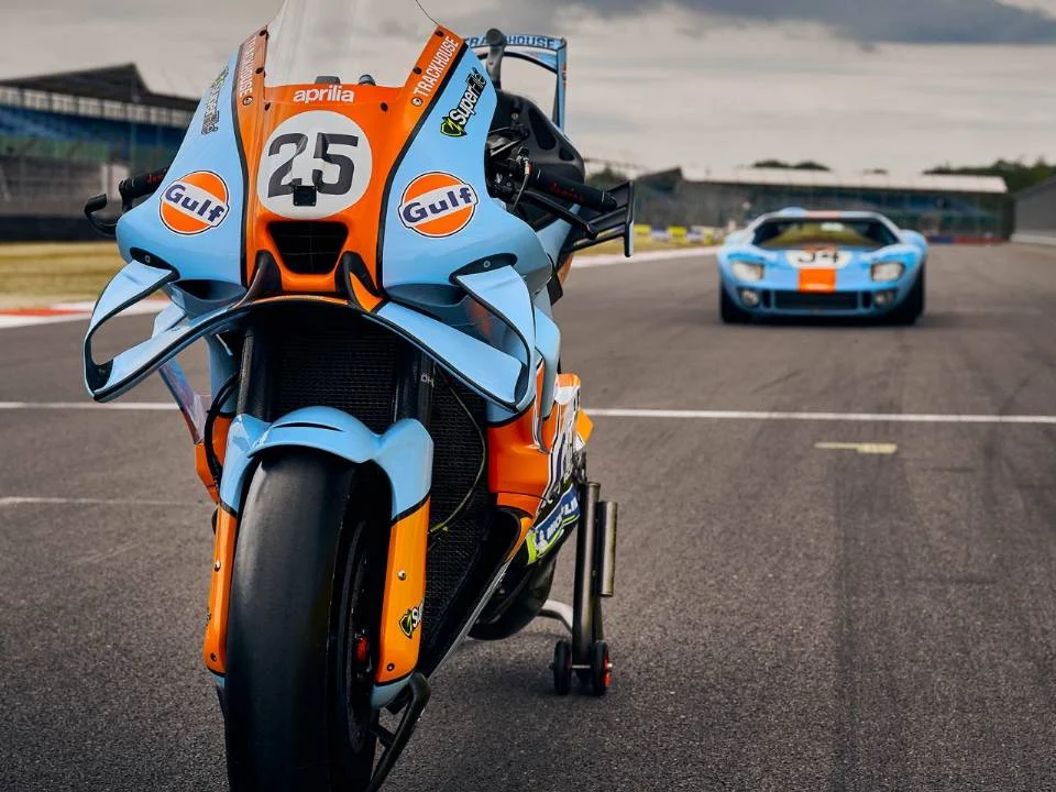 Aprilia RS-GP26 com pintura azul-claro e laranja inspirada na Ford GT40 em pista de MotoGP