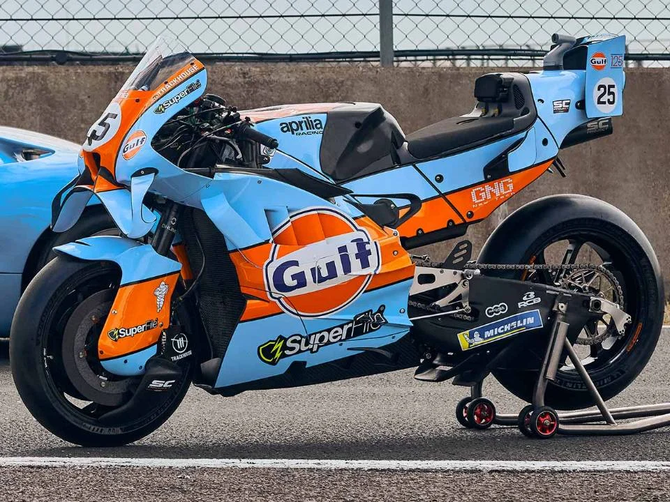 Aprilia RS-GP26 com pintura azul-claro e laranja inspirada na Ford GT40 em pista de MotoGP
