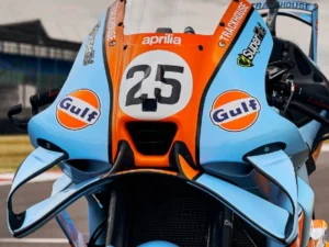 Aprilia RS-GP26 com pintura azul-claro e laranja inspirada na Ford GT40 em pista de MotoGP